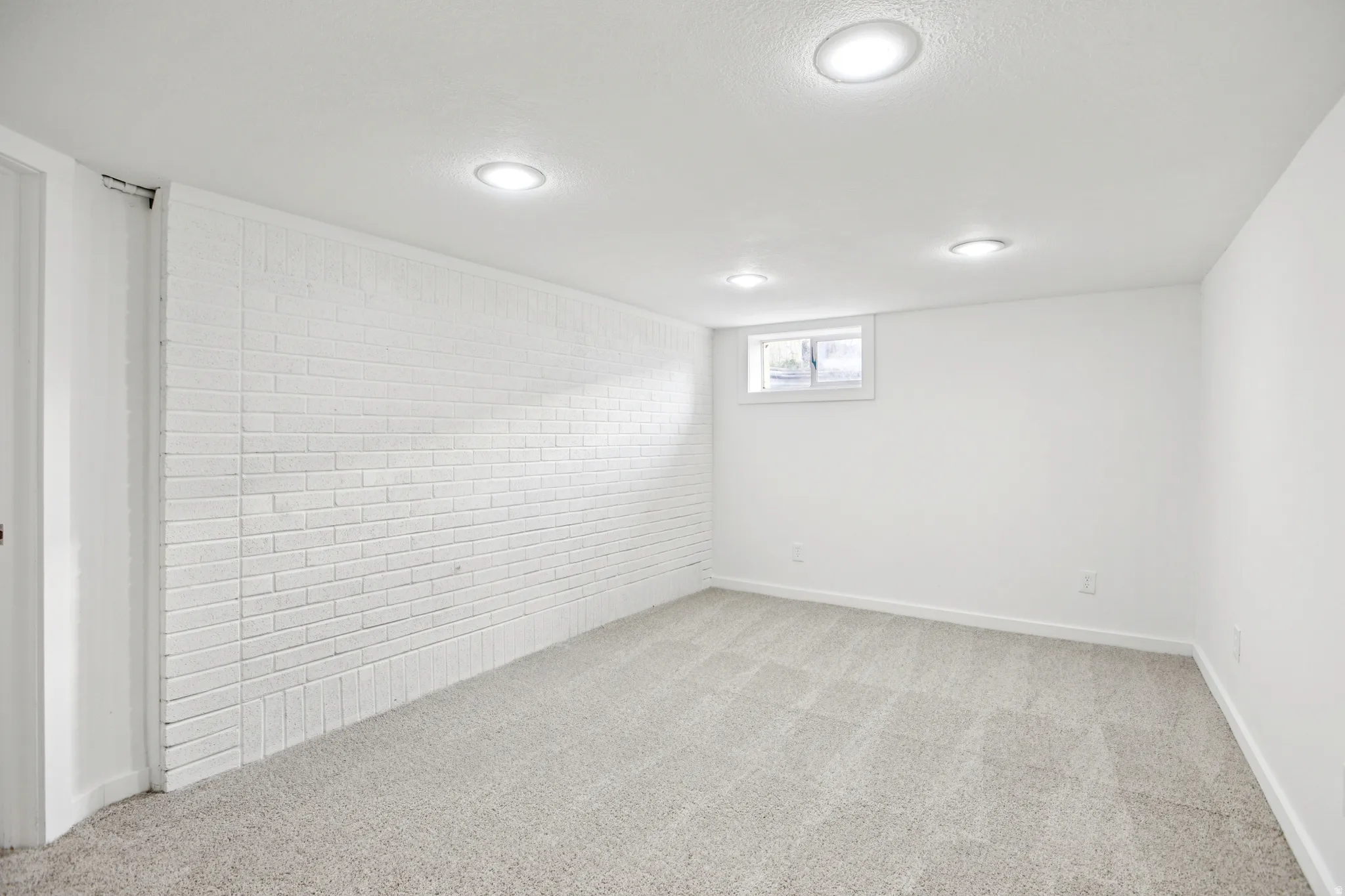 Below grade area with light colored carpet and brick wall