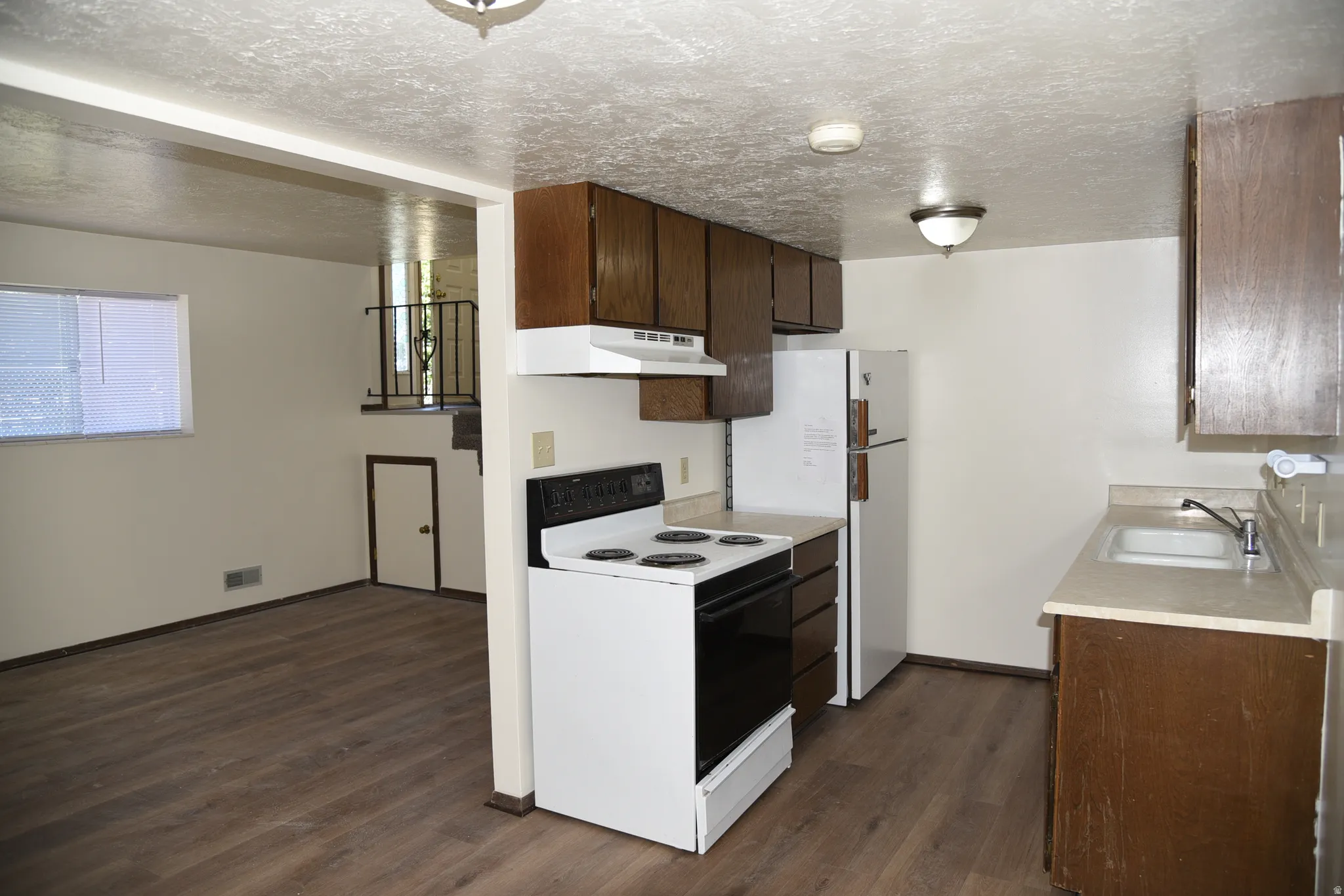 Kitchen area featuring wood-finish flooring, white appliances, and wood cabinetry