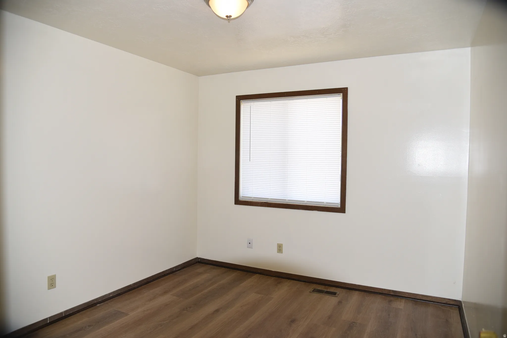 Room featuring neutral wall tones, wood-finish flooring, and a window with blinds