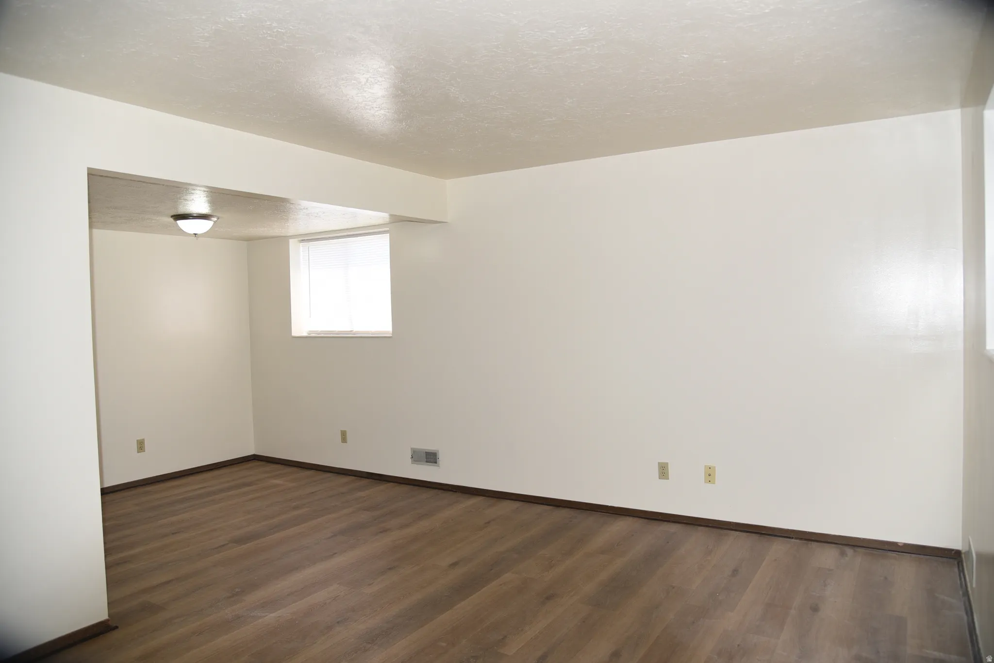 Interior room featuring wood-finish flooring, white walls, and a visible window with blinds
