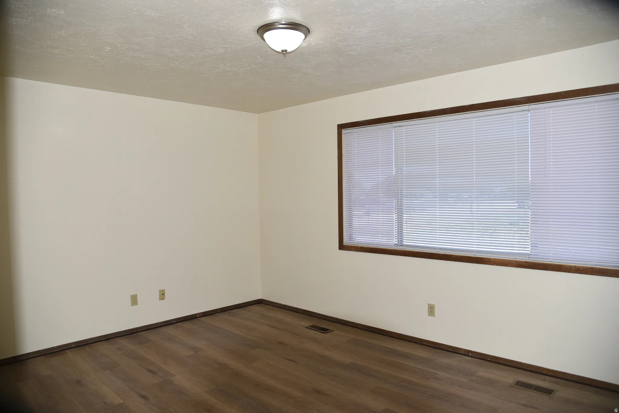Spacious room featuring wood-finish flooring, a large window with blinds, and neutral wall paint