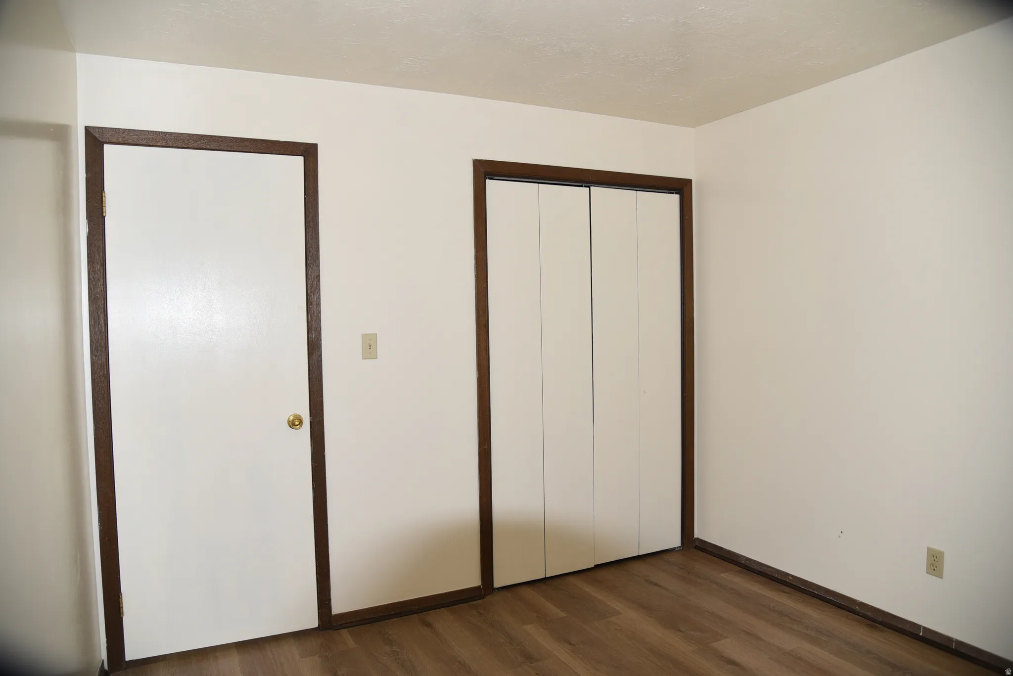 White walls featuring wood-finish flooring and dark wood trim