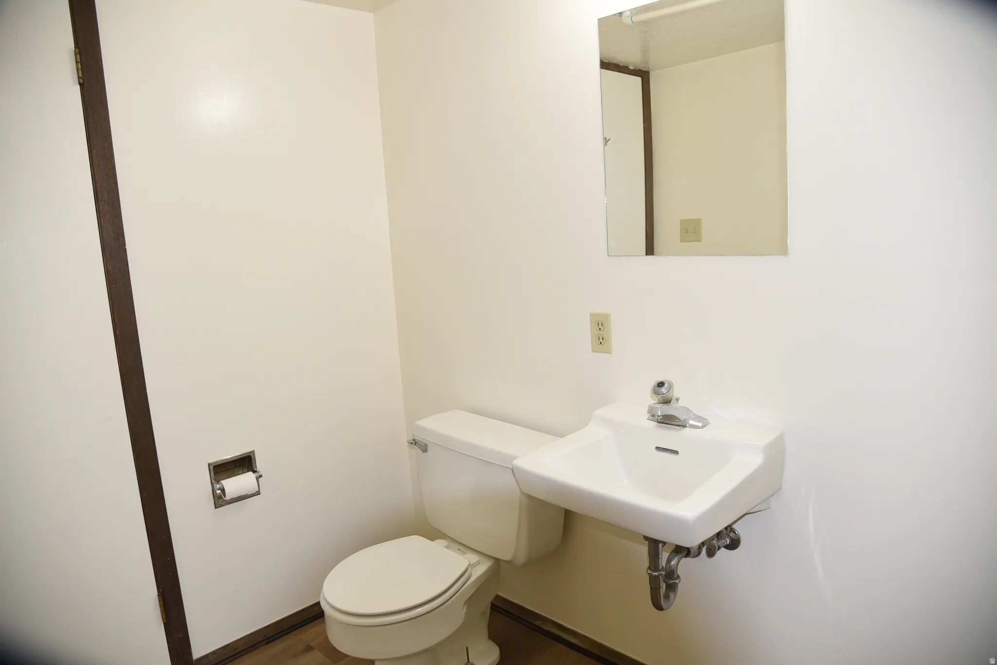 Wall-mounted sink with chrome faucet, white toilet, and mirror with overhead lighting