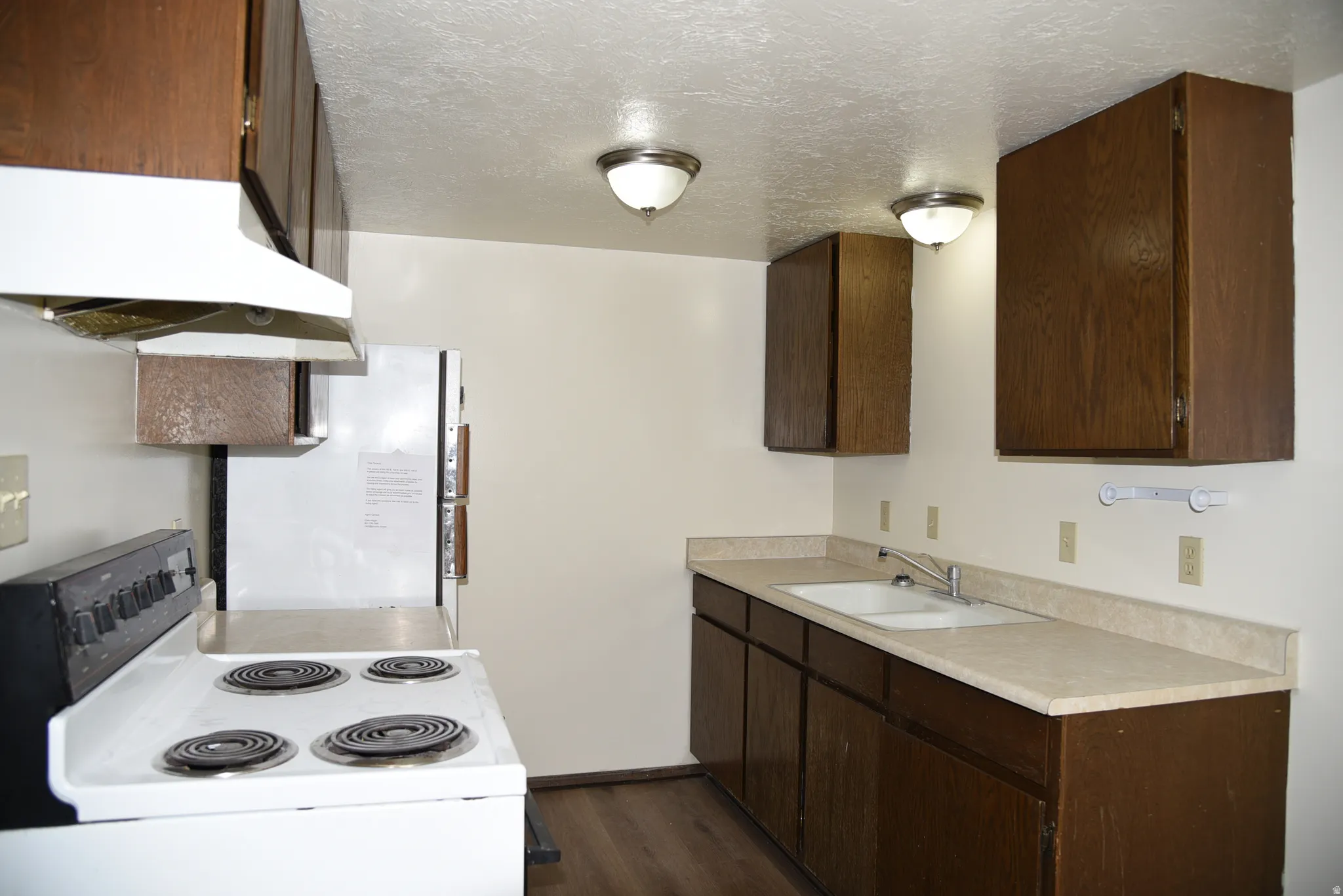 Kitchen featuring wood-finish cabinetry, a double basin sink, light-toned countertops, and wood-finish flooring