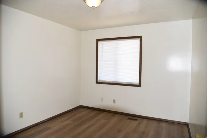 Room featuring neutral wall tones, wood-finish flooring, and a window with blinds