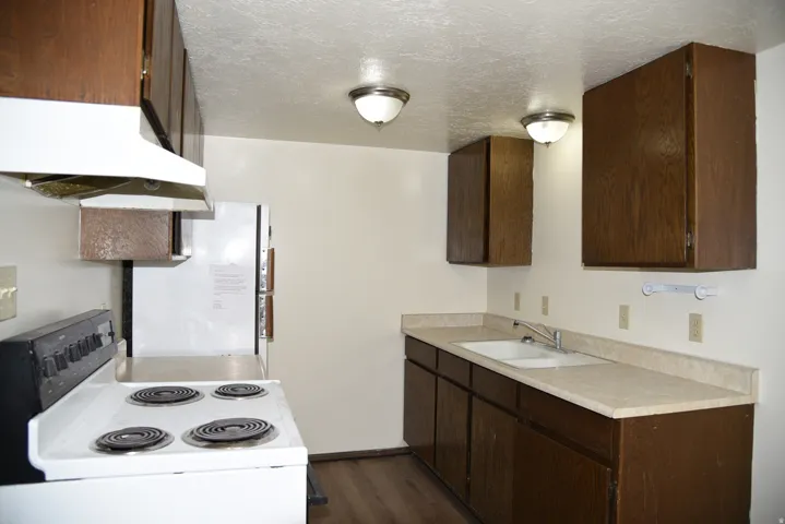 Kitchen featuring wood-finish cabinetry, a double basin sink, light-toned countertops, and wood-finish flooring
