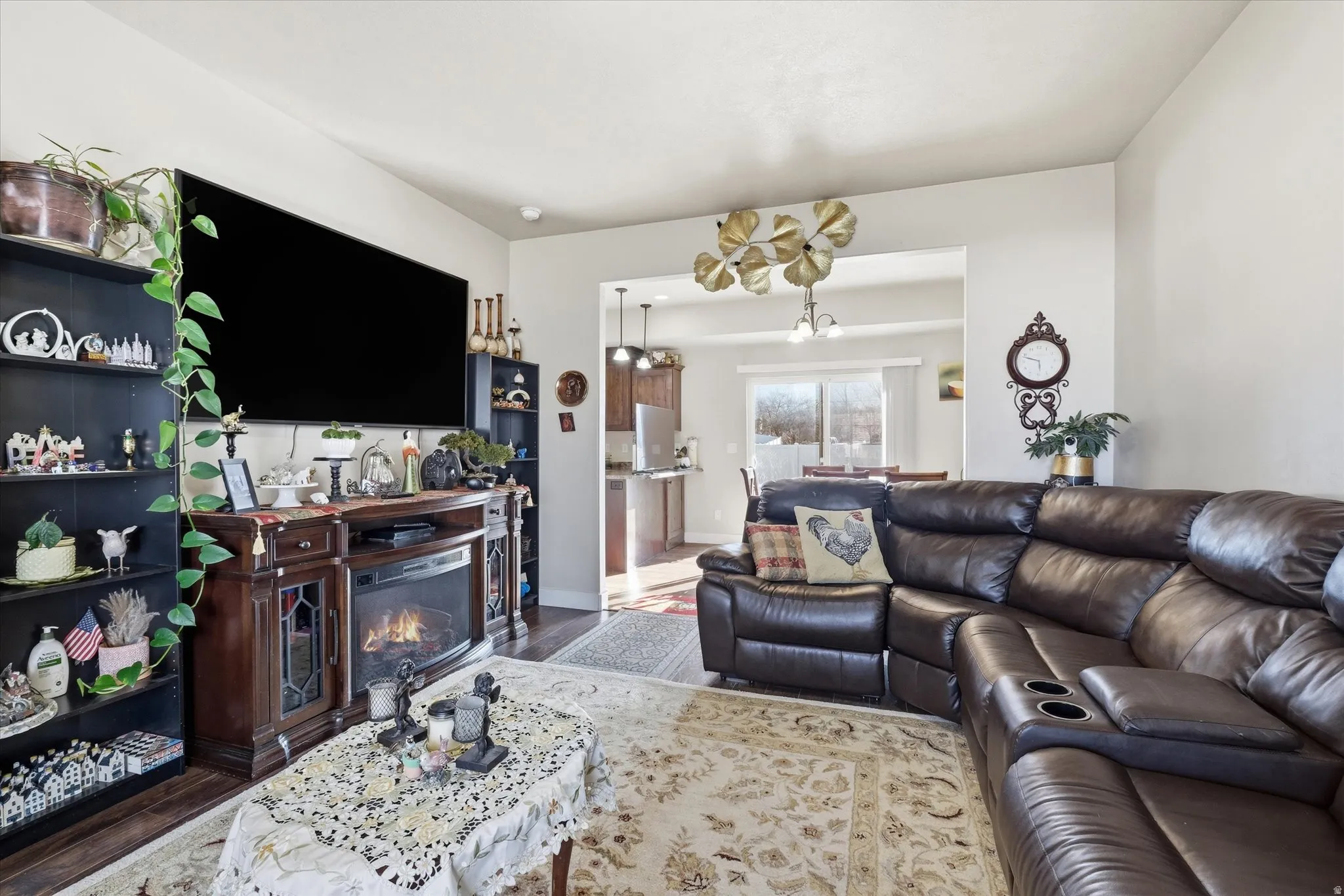 Living room with suspended lighting, wood finished floors, and a glass covered fireplace