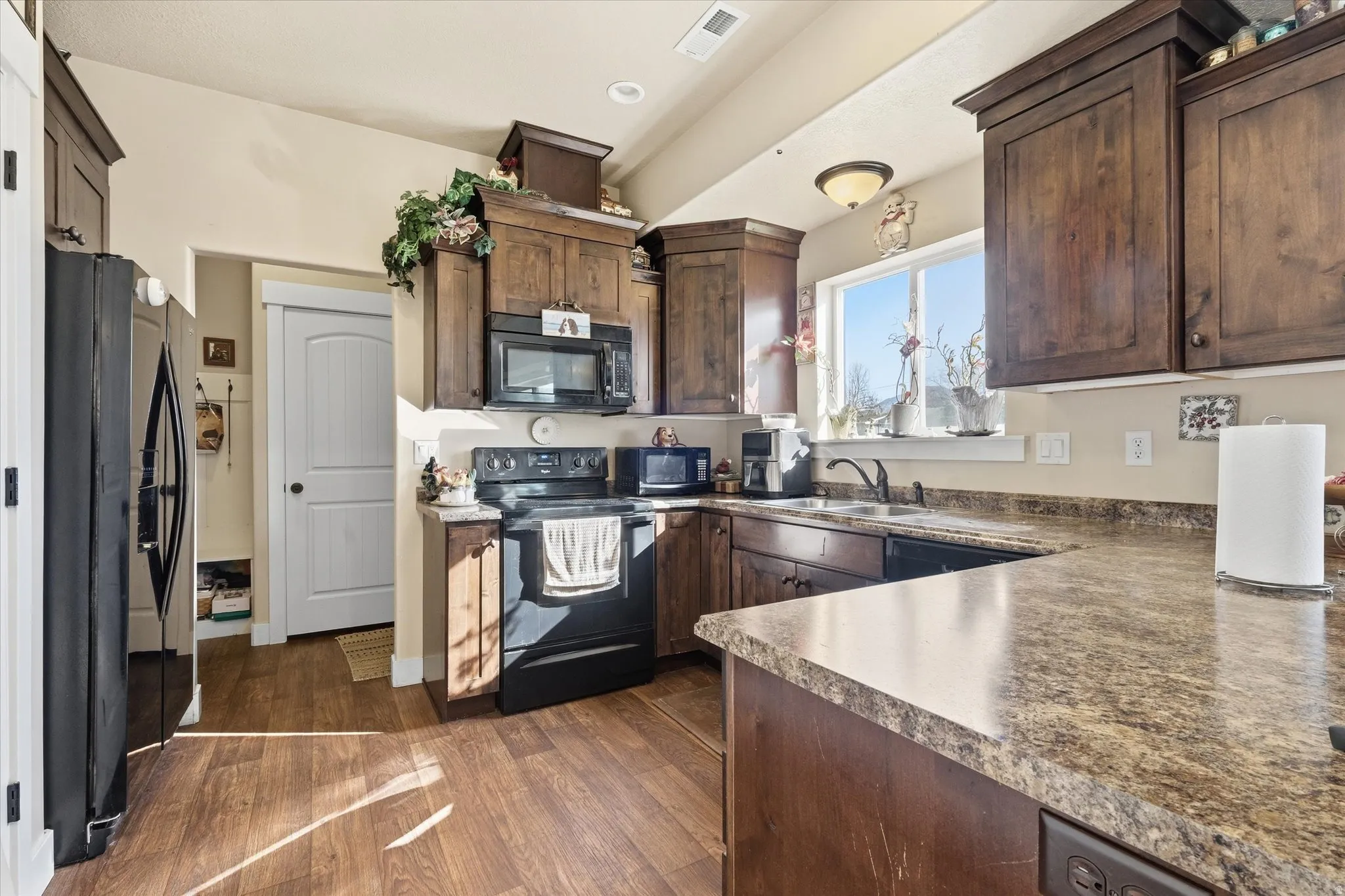 Kitchen featuring black appliances, dark wood finish cabinetry, dark wood-style floors, recessed lighting, and dark countertops