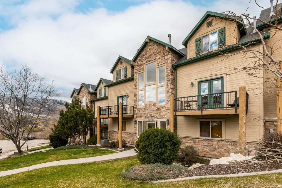 Rear view of property with stone siding, a balcony, and a lawn