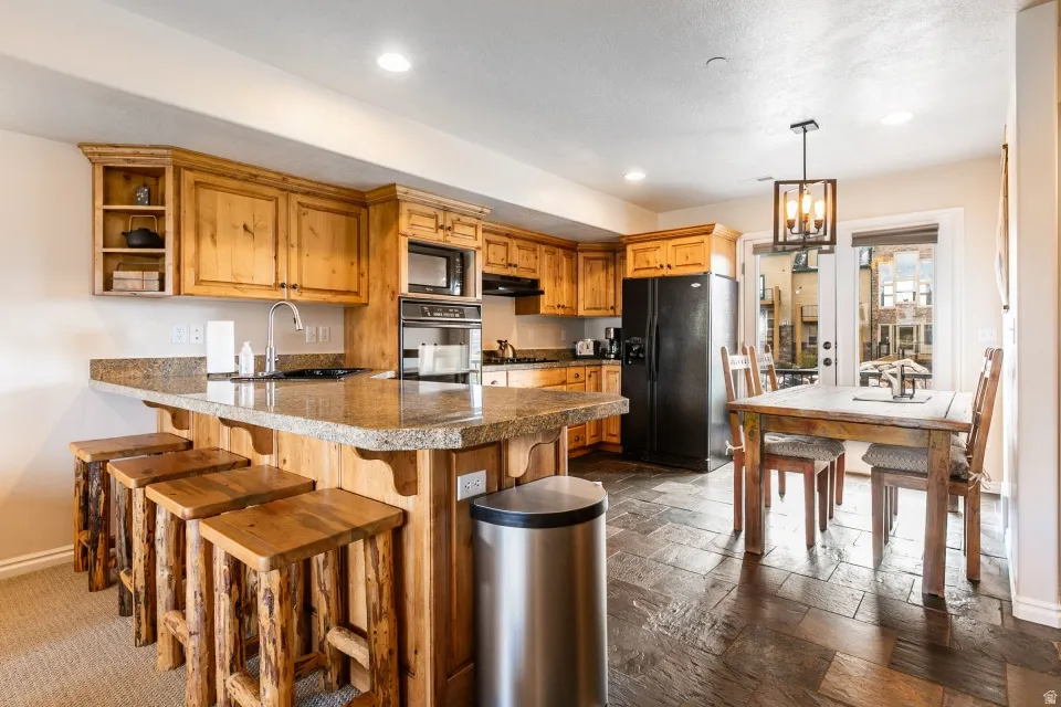 Kitchen with a peninsula, a kitchen bar, black appliances, wood finish cabinetry, and open shelves