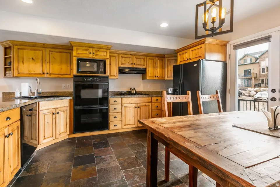 Kitchen with black appliances, stone tile flooring, dark countertops, open shelves, and wood finish cabinets
