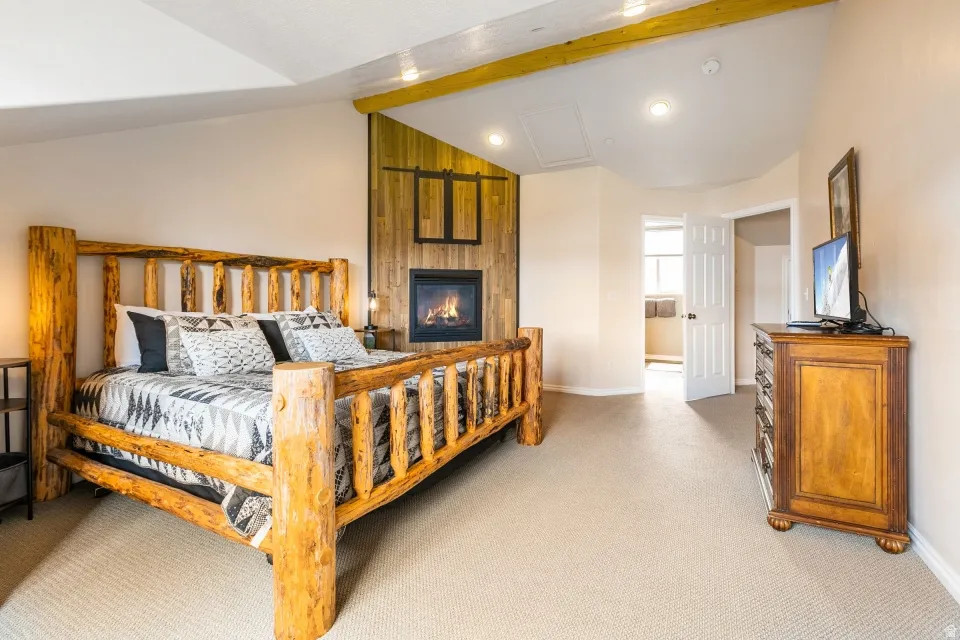 Bedroom featuring vaulted ceiling with beams, light colored carpet, and a fireplace