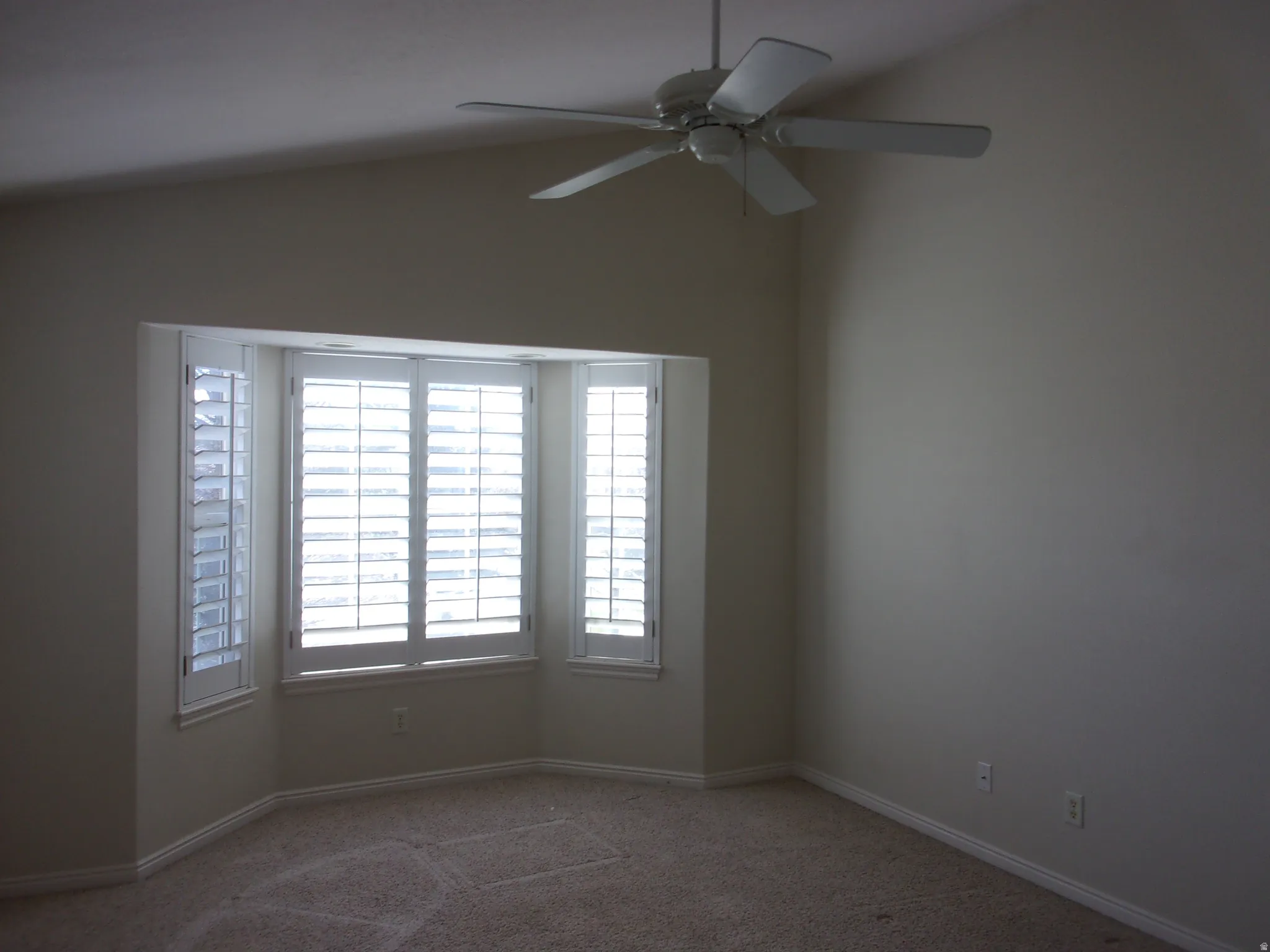 Carpeted spare room with vaulted ceiling and a ceiling fan