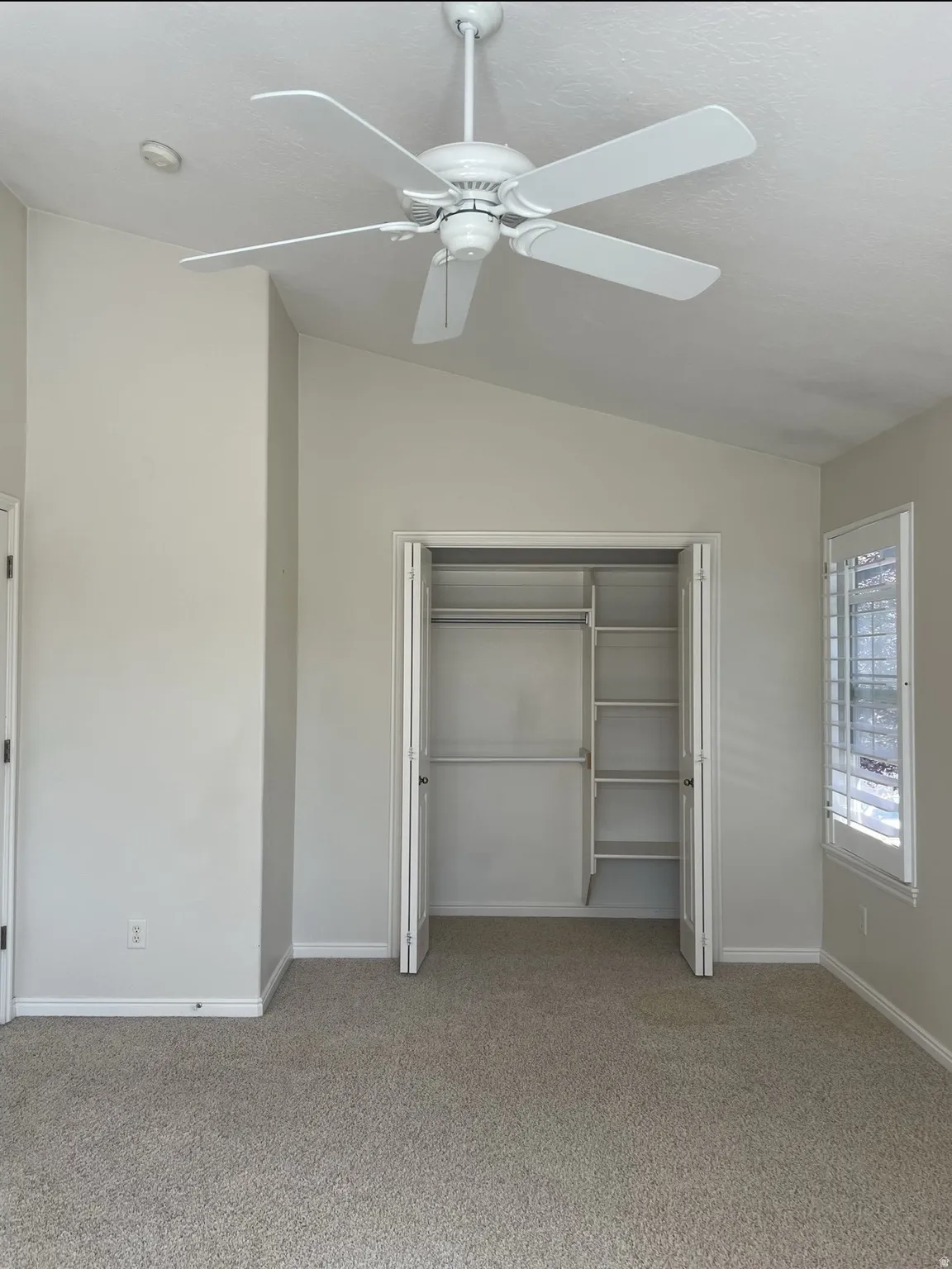 Unfurnished bedroom with vaulted ceiling, a closet, light carpet, and ceiling fan