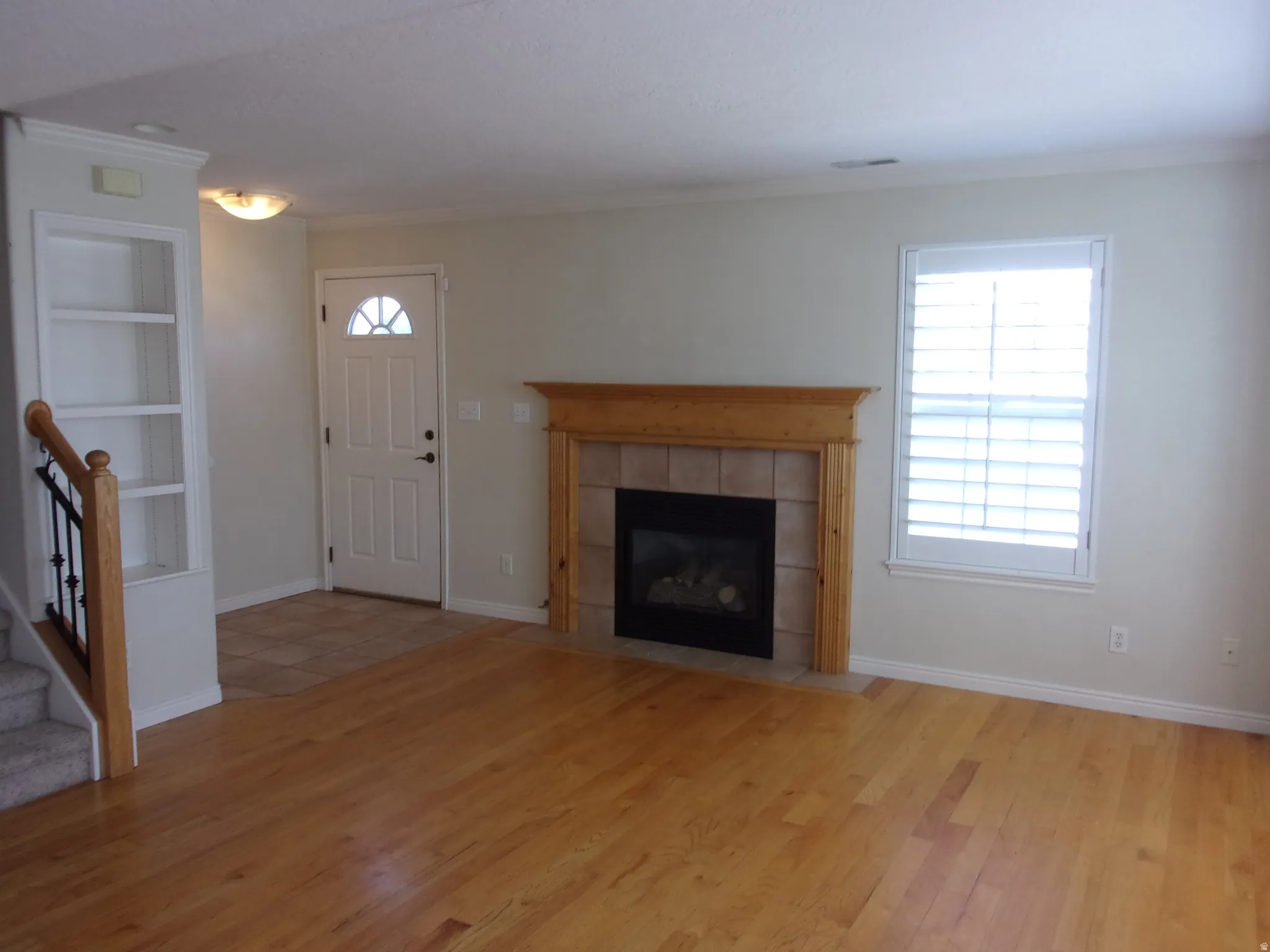 Unfurnished living room featuring built in shelves, light wood-style flooring, crown molding, and plenty of natural light
