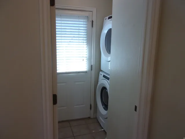Laundry room with light tile patterned flooring and stacked washing machine and dryer