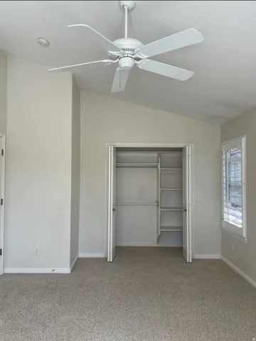 Unfurnished bedroom with vaulted ceiling, a closet, light carpet, and ceiling fan