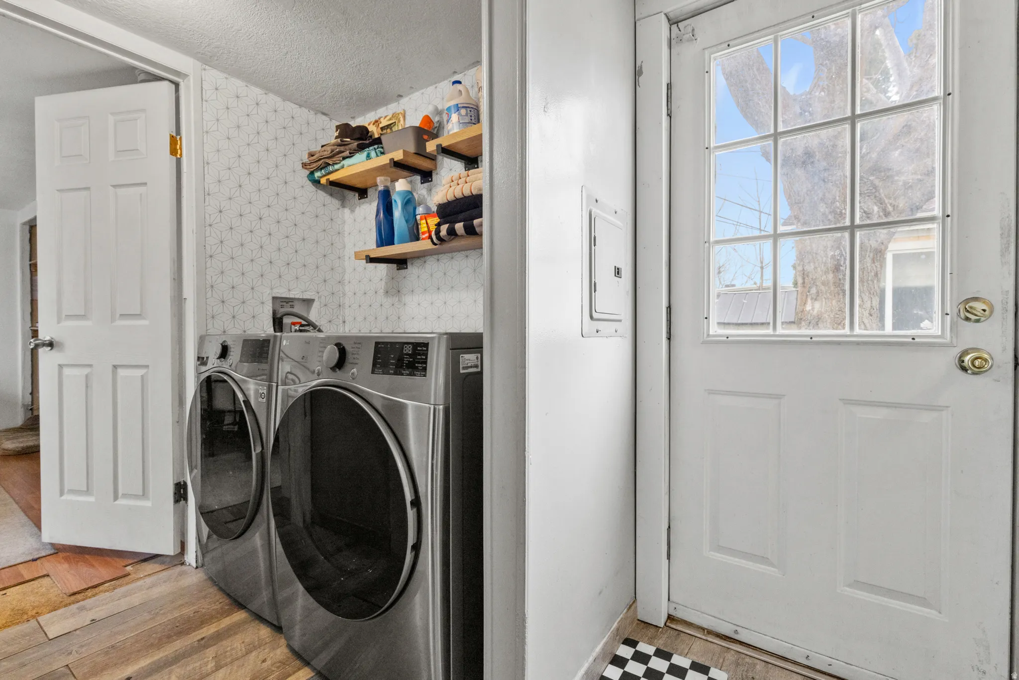 Laundry room featuring wallpapered walls, washing machine and clothes dryer, a textured ceiling, electric panel, and light wood-type flooring