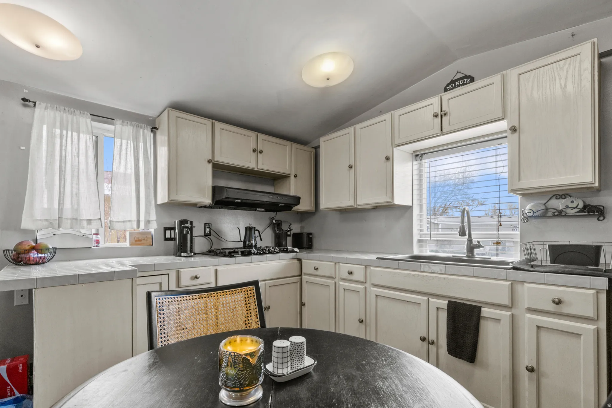 Kitchen with tile countertops, lofted ceiling, gas stovetop, and cream cabinets