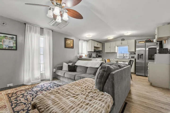 Living area featuring a ceiling fan, lofted ceiling, and light wood-style flooring