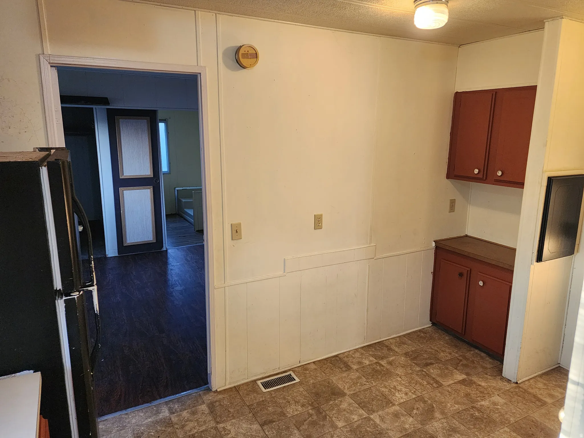 Kitchen with wainscoting, freestanding refrigerator, dark countertops, stone finish floors, and a decorative wall