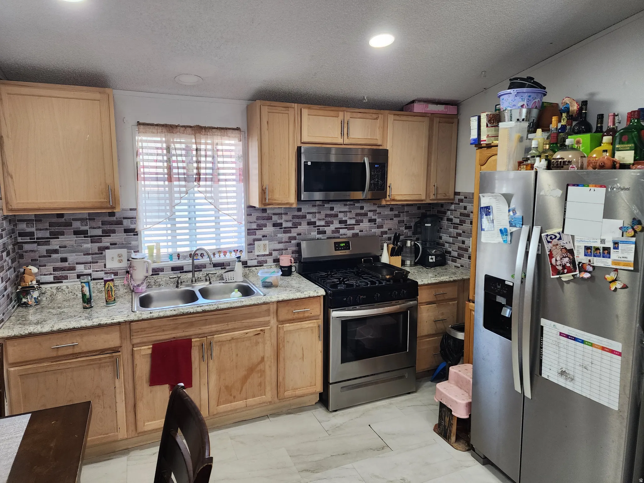Kitchen featuring stainless steel appliances, tasteful backsplash, light stone countertops, light marble finish floors, and a textured ceiling