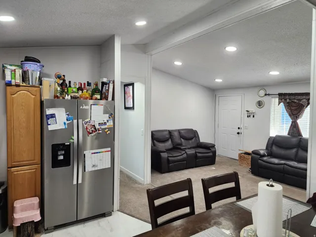 Kitchen with a textured ceiling, stainless steel refrigerator with ice dispenser, recessed lighting, light carpet, and open floor plan