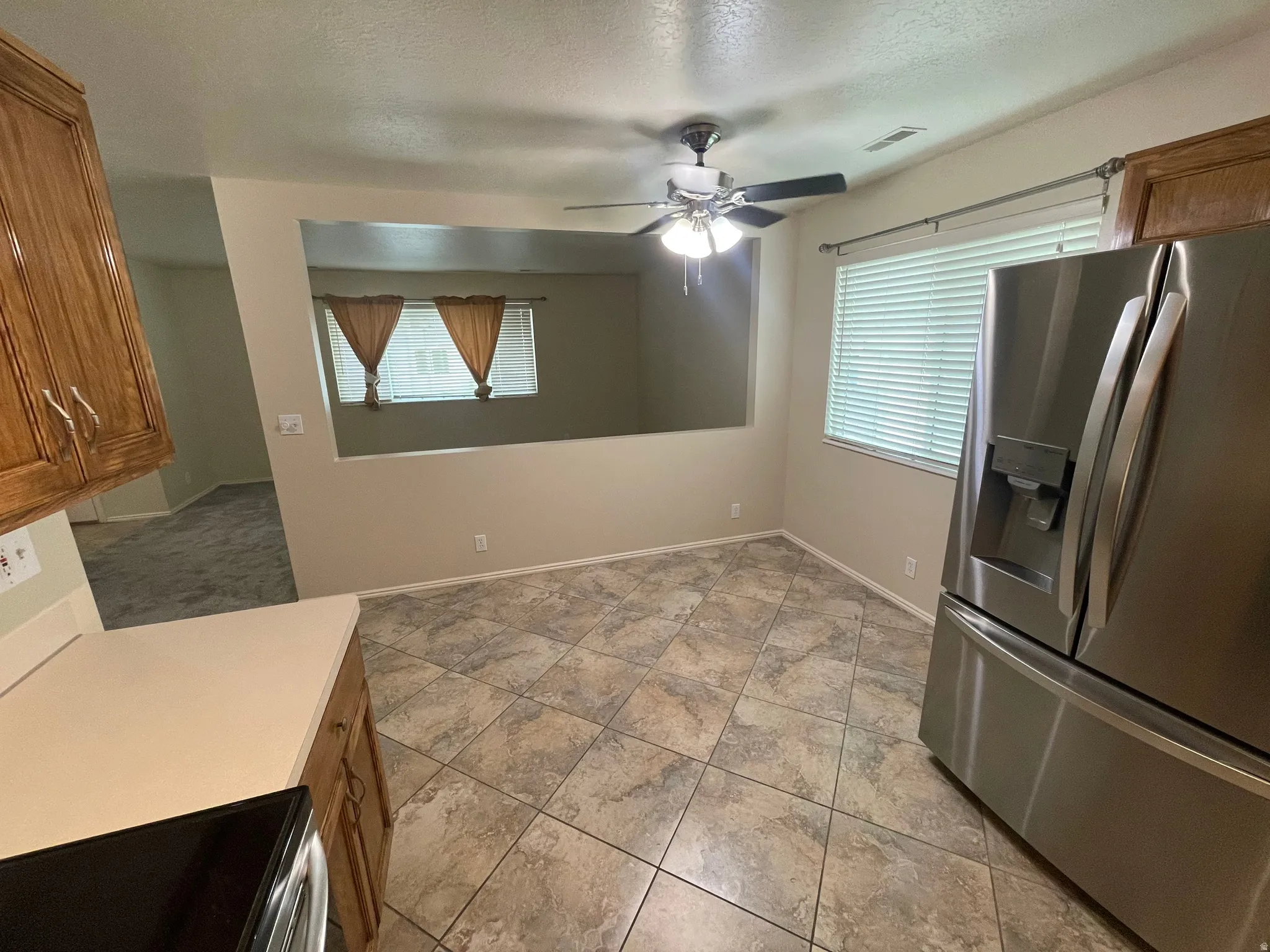 Kitchen featuring stainless steel fridge with ice dispenser, wood finish cabinetry, stove, light countertops, and ceiling fan