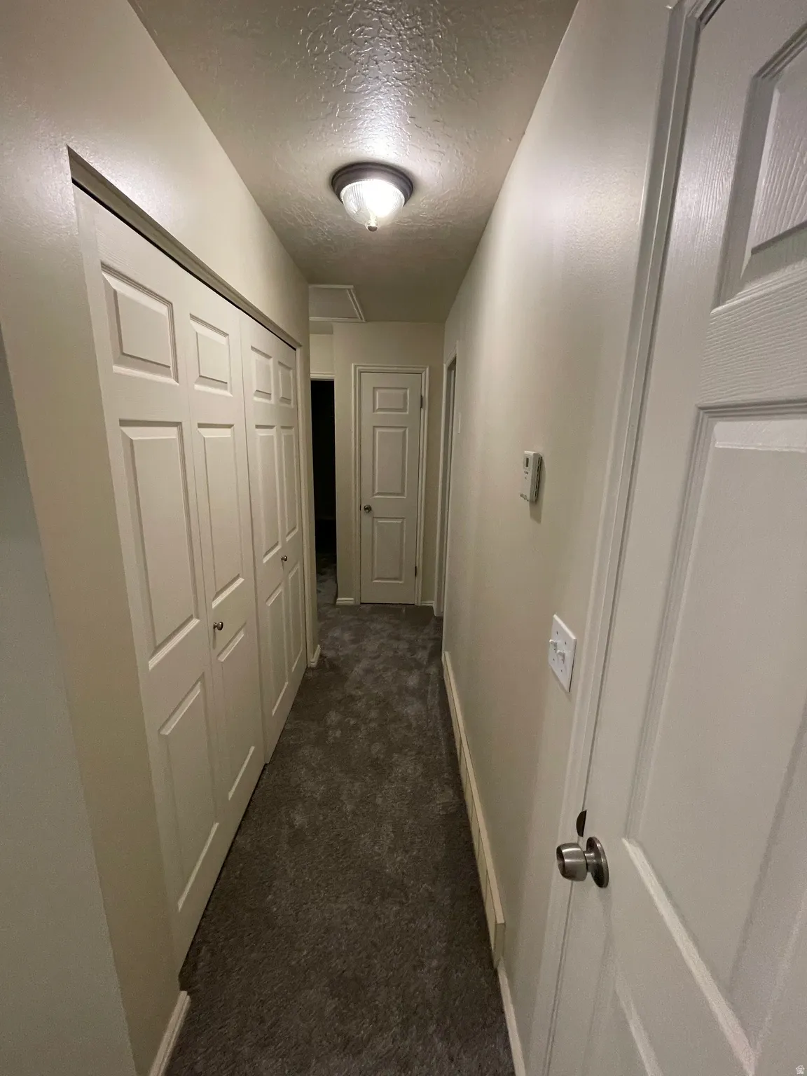 Corridor featuring a textured ceiling and dark carpet