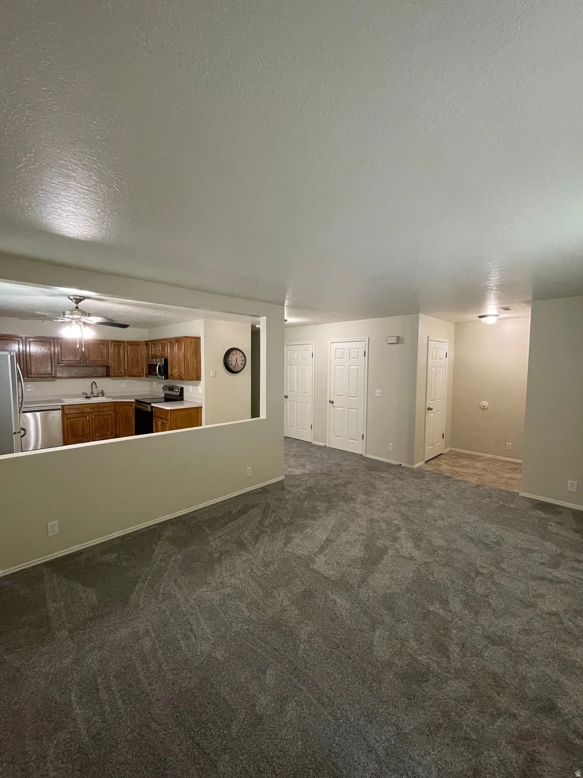 Unfurnished living room with a textured ceiling, dark carpet, and a ceiling fan