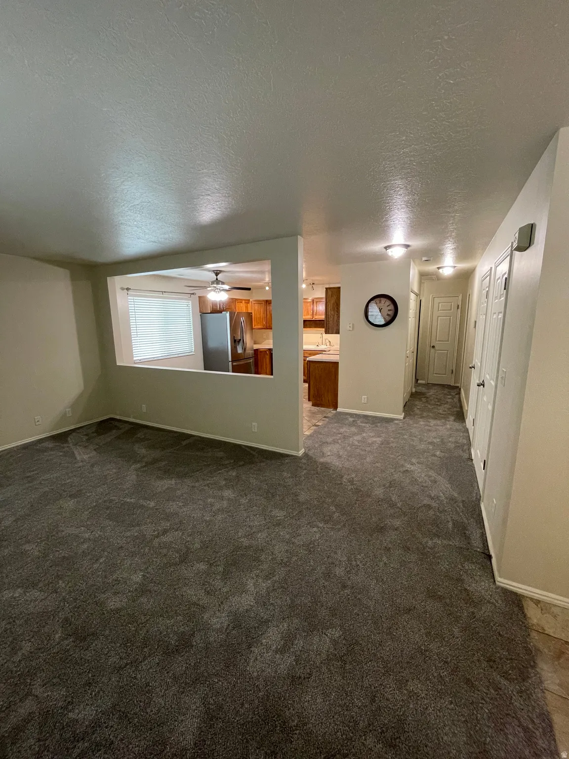 Empty room with a textured ceiling, dark carpet, and a ceiling fan