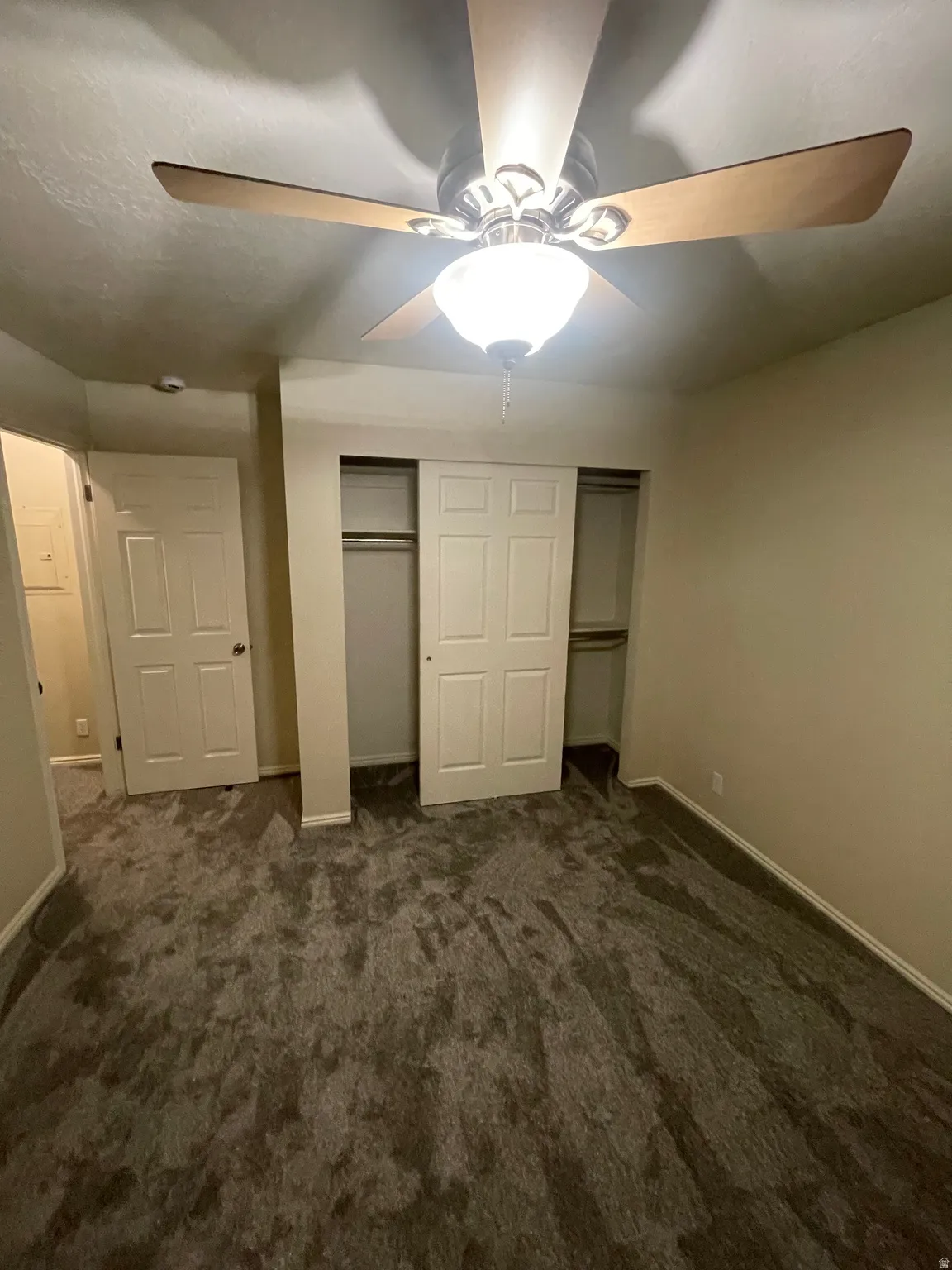 Unfurnished bedroom with dark carpet, a closet, and a ceiling fan