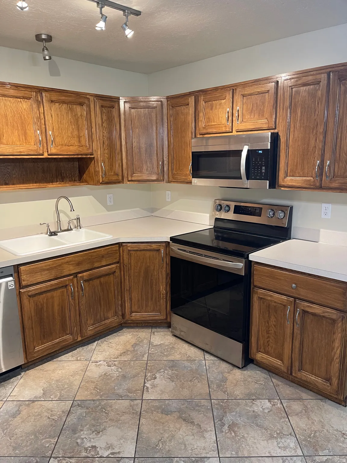 Kitchen featuring stainless steel appliances, light countertops, wood finish cabinetry, and rail lighting