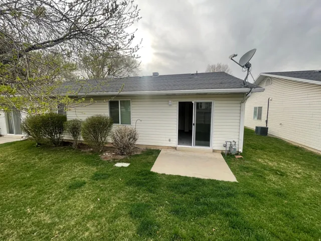 Rear view of house featuring a patio area, a lawn, and a shingled roof