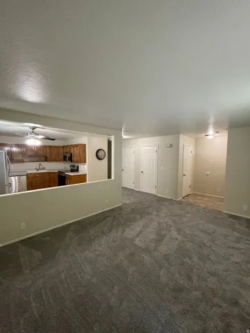 Unfurnished living room with a textured ceiling, dark carpet, and a ceiling fan