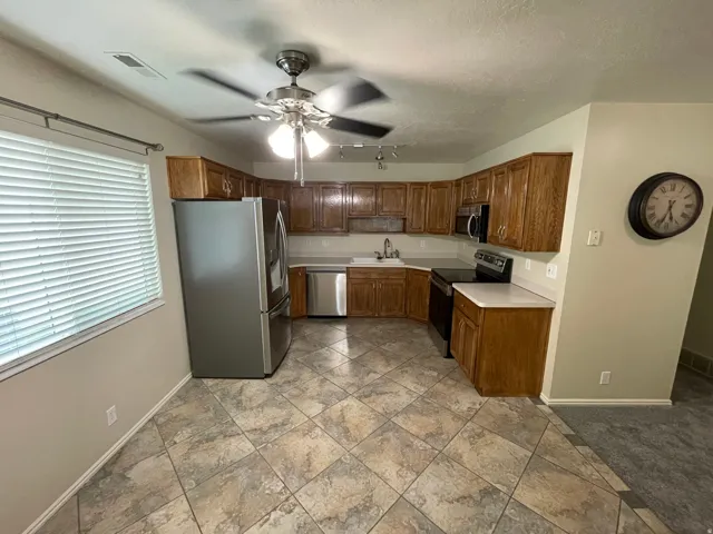 Kitchen with stainless steel appliances, light countertops, ceiling fan, wood finish cabinetry, and a textured ceiling