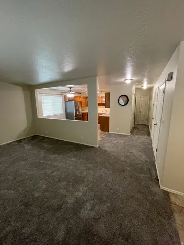 Empty room with a textured ceiling, dark carpet, and a ceiling fan