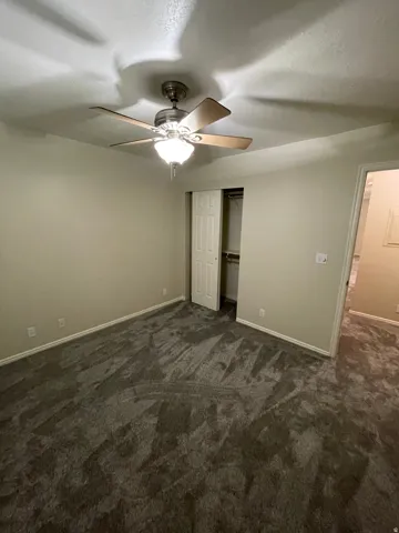 Unfurnished bedroom featuring a closet, dark carpet, and a ceiling fan
