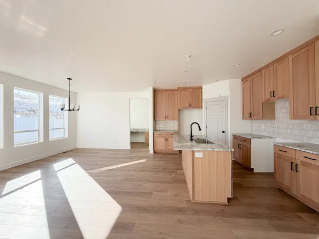Kitchen featuring a kitchen island with sink, light wood-style floors, a chandelier, open floor plan, and light stone counters
