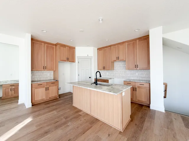 Kitchen featuring a kitchen island with sink, light stone countertops, light wood finished floors, light wood finish cabinetry, and recessed lighting