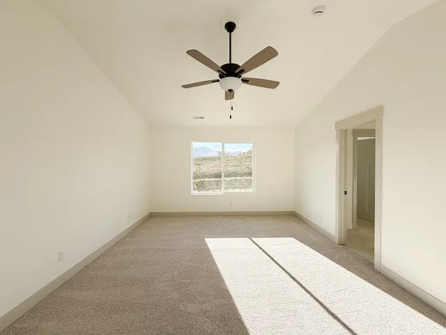 Primary bedroom with light carpet, vaulted ceiling, and ceiling fan