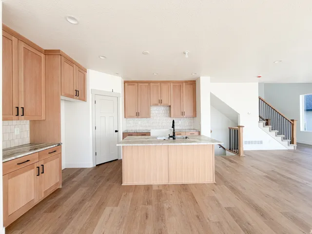 Kitchen featuring light wood finish cabinets, light wood-style flooring, light stone countertops, an island with sink, and recessed lighting