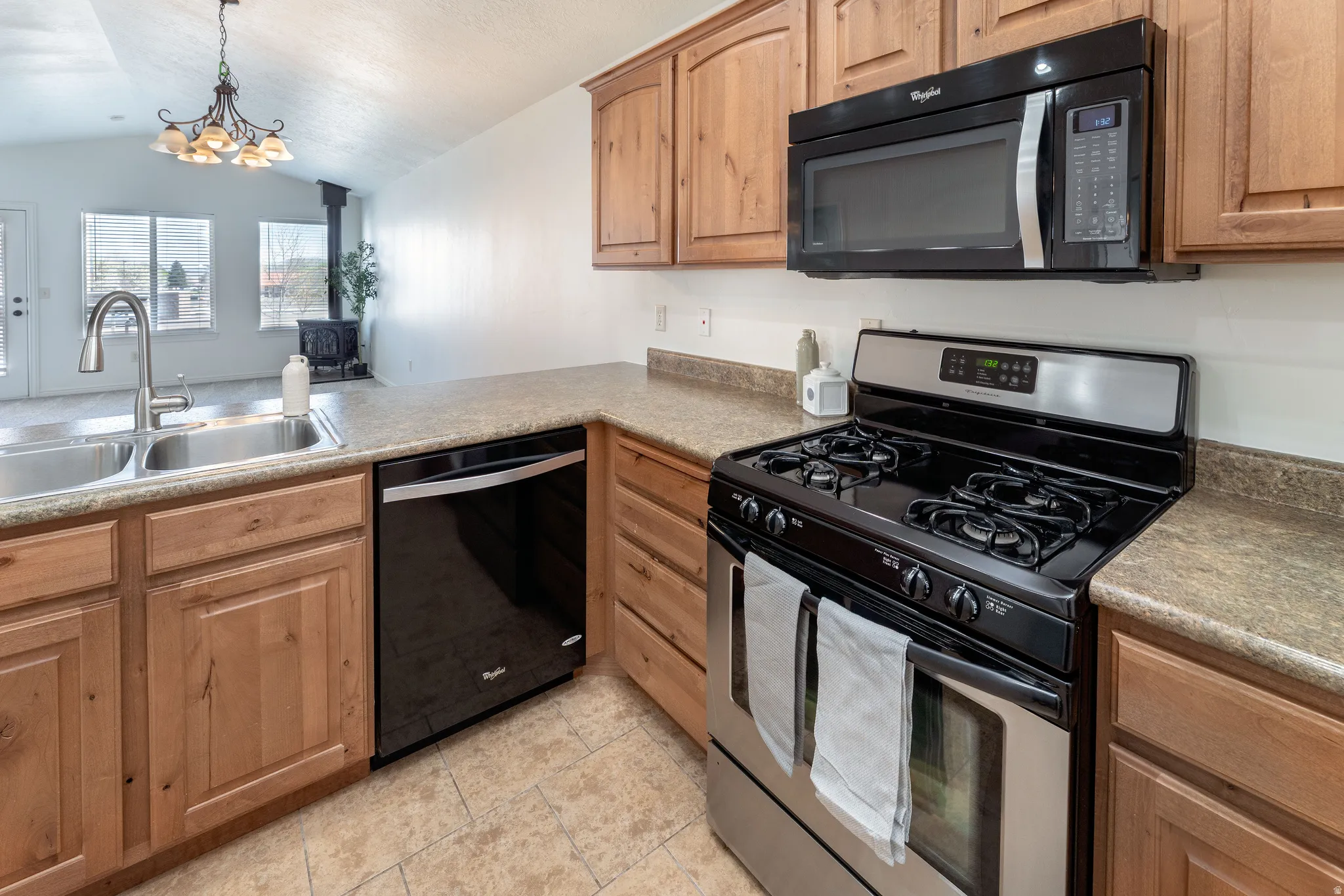 Kitchen with black appliances, hanging lights, vaulted ceiling, light tile patterned floors, and light countertops