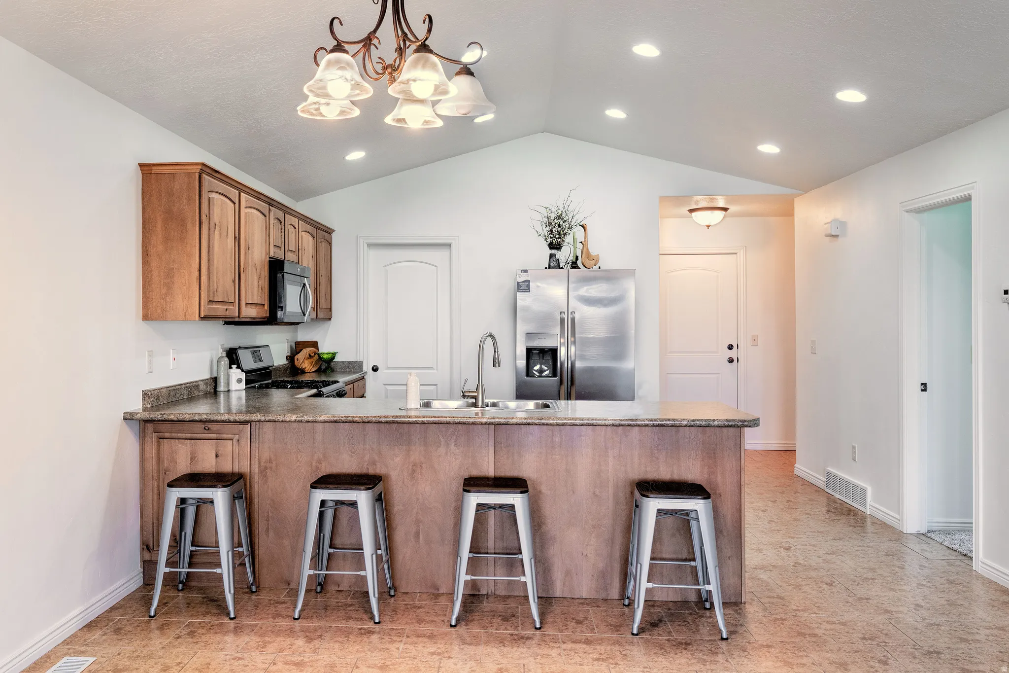 Kitchen with a peninsula, stainless steel fridge with ice dispenser, a breakfast bar area, range with gas cooktop, and wood finish cabinetry