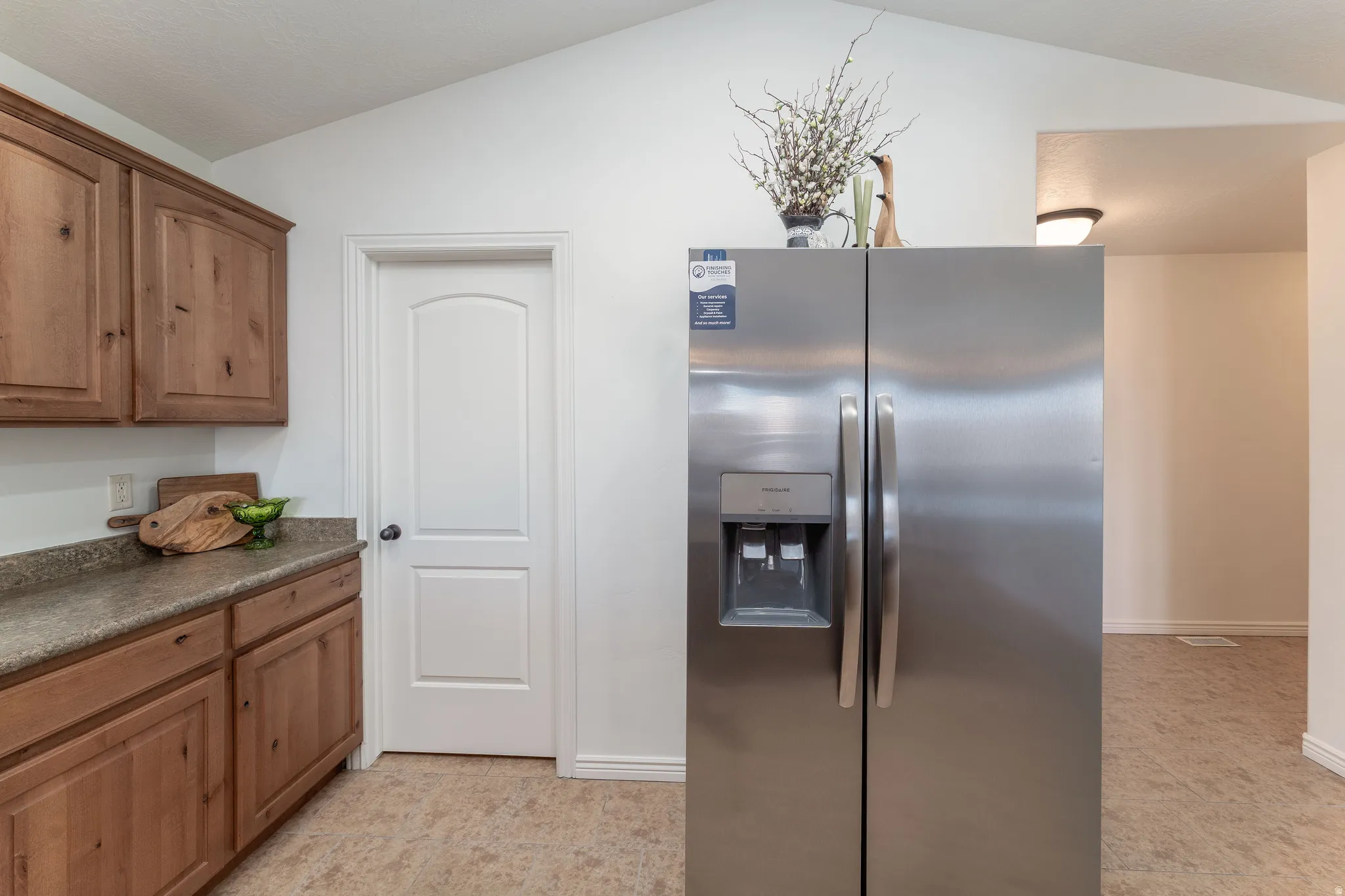 Kitchen featuring stainless steel fridge, dark countertops, vaulted ceiling, and wood finish cabinets
