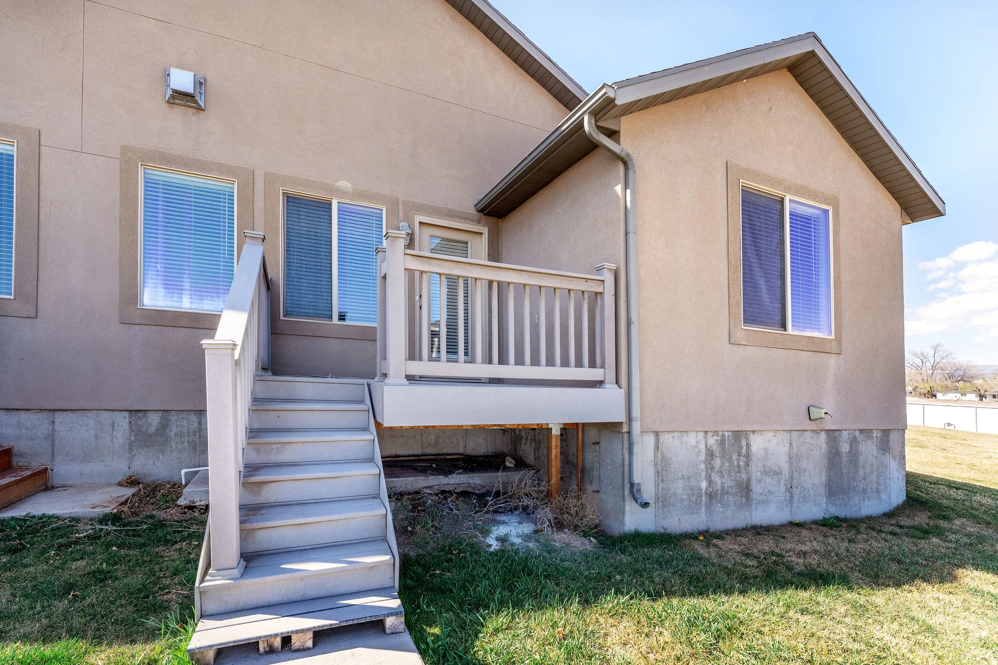 View of exterior entry featuring stucco siding, a wooden deck, and a lawn