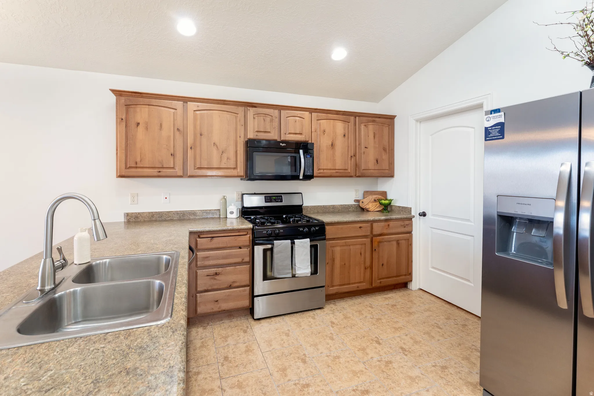 Kitchen featuring stainless steel appliances, vaulted ceiling, light countertops, and recessed lighting