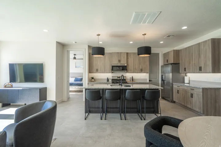 Kitchen featuring light stone countertops, a breakfast bar area, an island with sink, hanging light fixtures, and stainless steel appliances