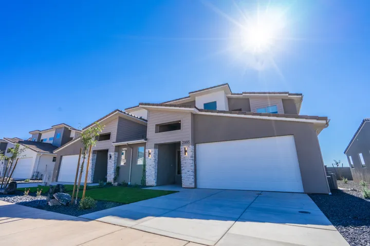 View of front facade featuring an attached garage, concrete driveway, stone siding, and stucco siding