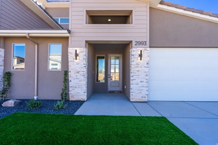 Entrance to property with stone siding, stucco siding, french doors, concrete driveway, and a yard